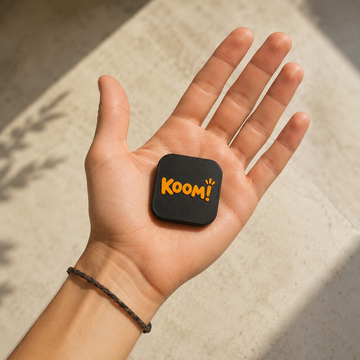 תג Koom! מונח על כף יד - בערך בגודל של קופסת גפרורים